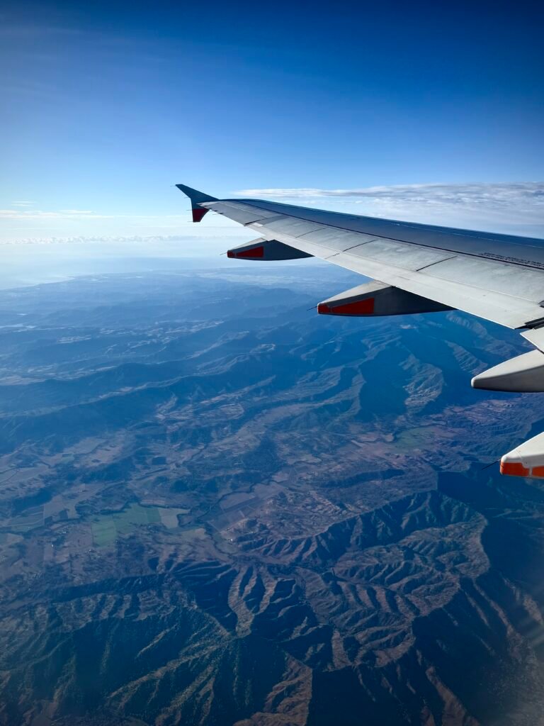 Looking out an airplane window with mountains below and blue skies