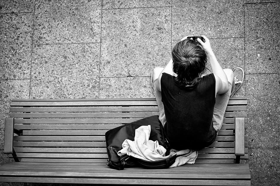 Black and white image of teenage boy on bench holding a mobile phone